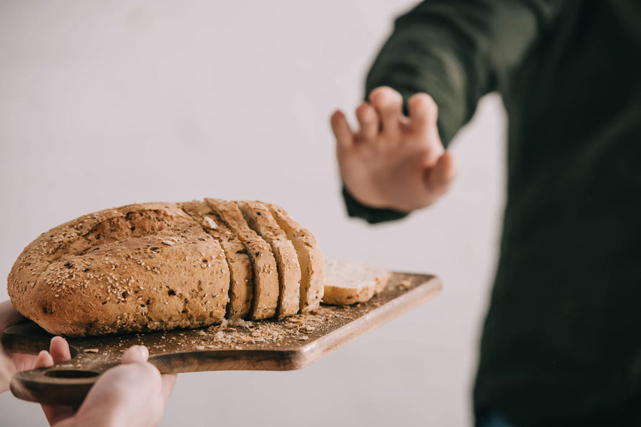 Hand wehrt Brotangebot ab – Schneidebrett mit aufgeschnittenem Vollkornbrot im Vordergrund